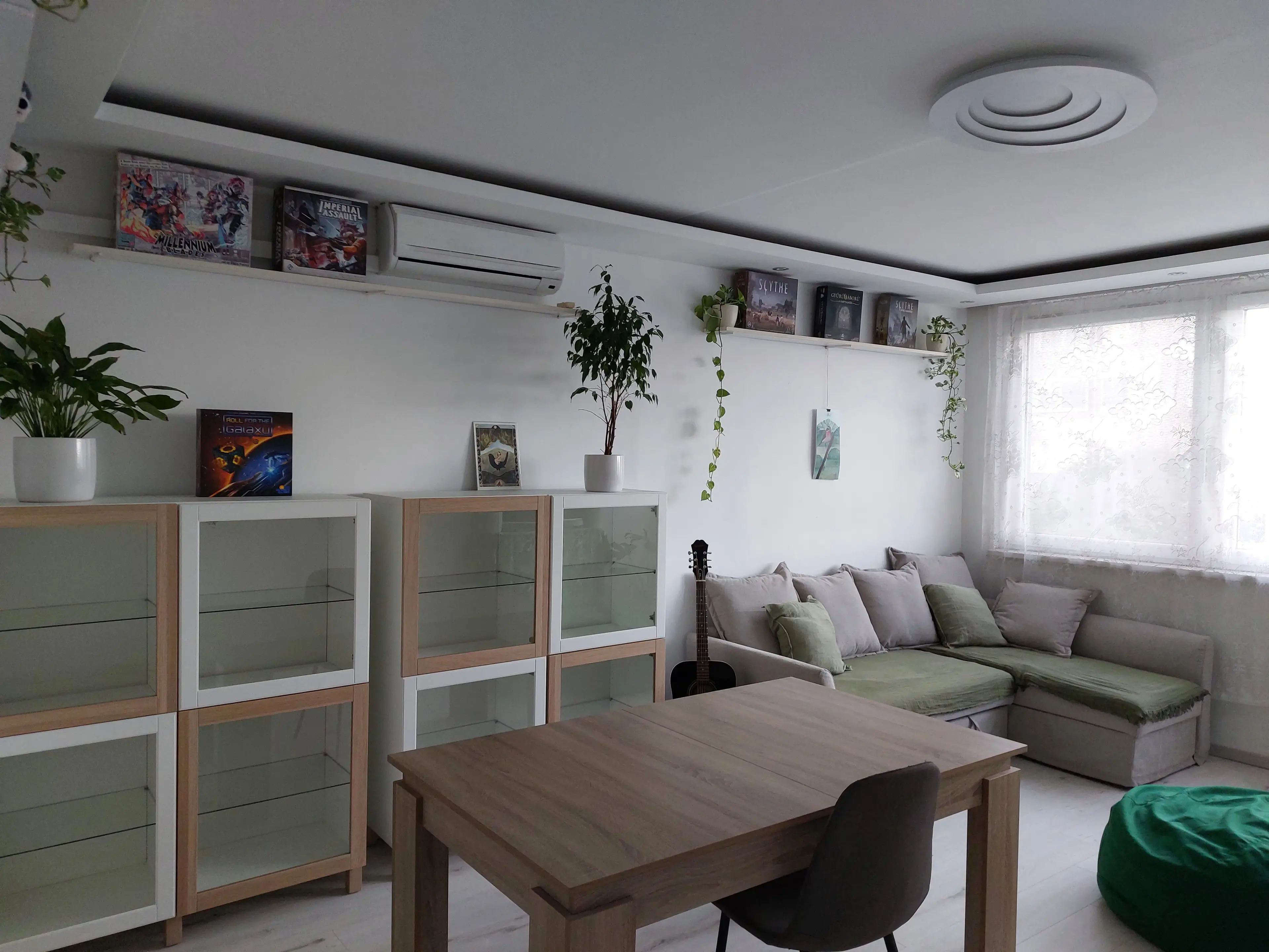 Egy szoba, középen egy gitár, hátul kanapé, polcokon társasjátékok, elől asztal, jobbra babzsákfotel